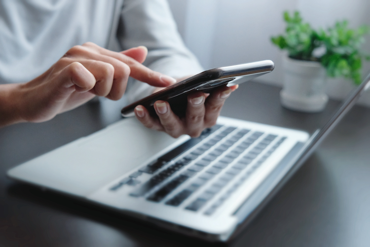 Closeup of hand using a smartphone with laptop