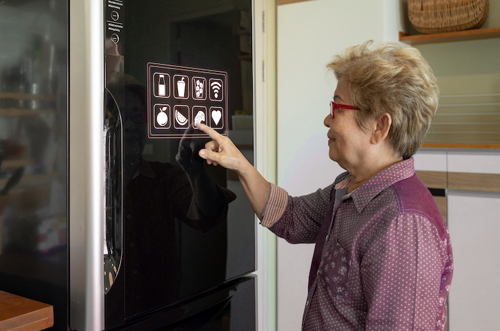 Elderly woman touching control panel of smart refrigerator
